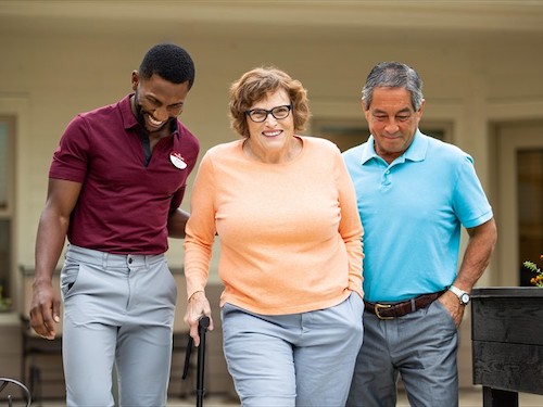 Primrose staff member guiding resident on a walk outdoors and her husband also assisting