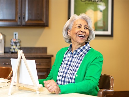 Primrose Memory Care resident smiling as she paints on a canvas