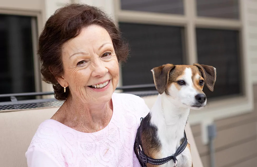 A Primrose resident smiling while sitting outside with her dog on her lap