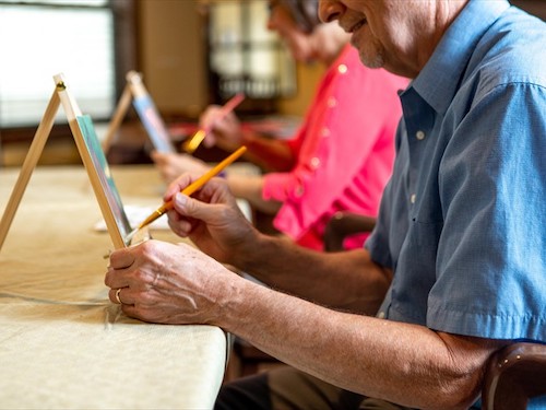 Primrose Memory Care residents painting on canvases while seated at a table