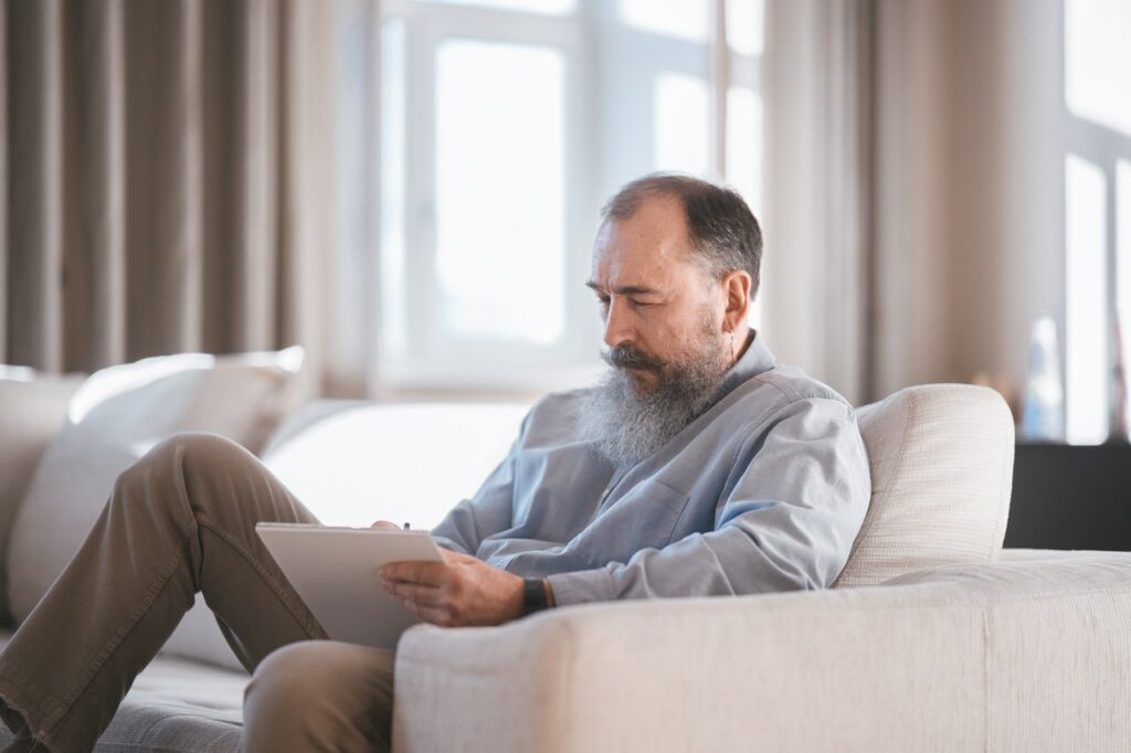Older man siting on a couch with clipboard