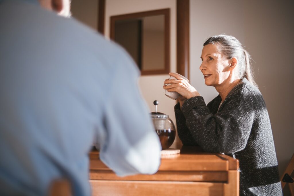 Older woman sitting at kitchen table with husband enjoying a cup of morning coffee.