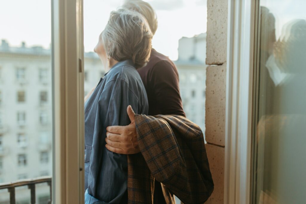 A husband and wife staring out of window on balcony.