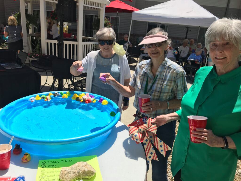 Three senior women playing at activities table outside during event.