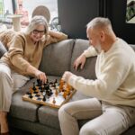 An elderly couple playing chess in their retirement home.