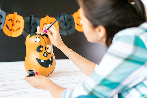 Woman painting silly face on pumpkin squash.