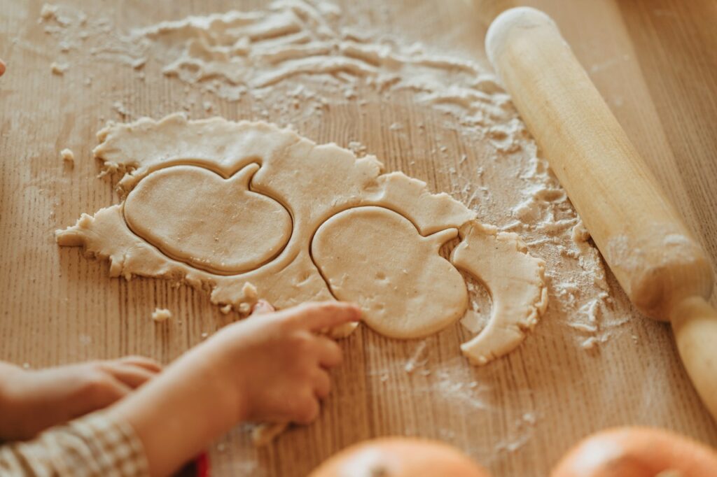 Little boy helping grandma making pumpkin-shaped cookies.