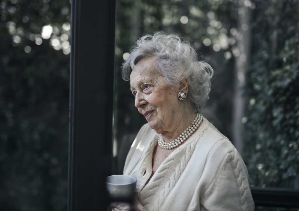 Elderly woman staring out window of home.