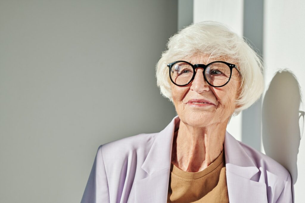 Senior woman with glasses wearing stylish purple jacket.