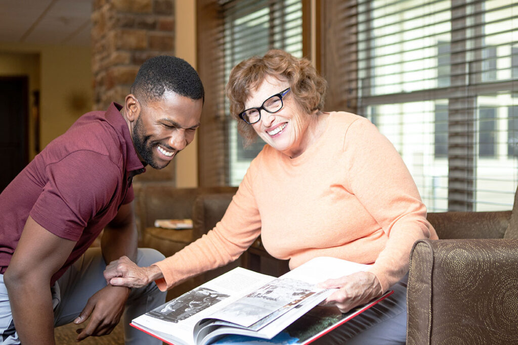 Primrose staff member laughing with resident as they look at a book together.