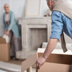 side view of senior man holding cardboard box and helping wife pack things