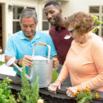 Memory care residents spending time doing gardening in the outdoor courtyard with a helpful staff member