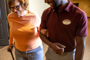 Staff member guiding a female resident as they walk down the hall together.