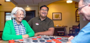 Two senior residents playing checkers while they share a laugh with a staff member