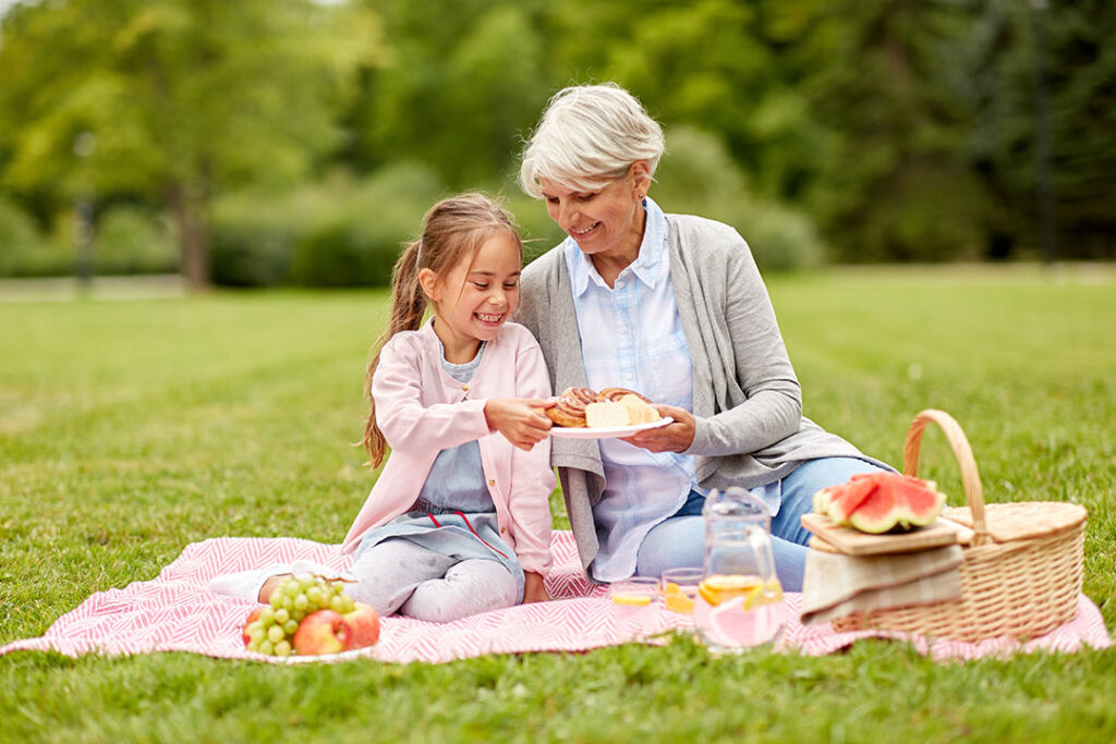 A grandma having a picnic with her granddaughter in the grass and eating snacks.