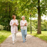 Two senior ladies walking in the park with their coffees