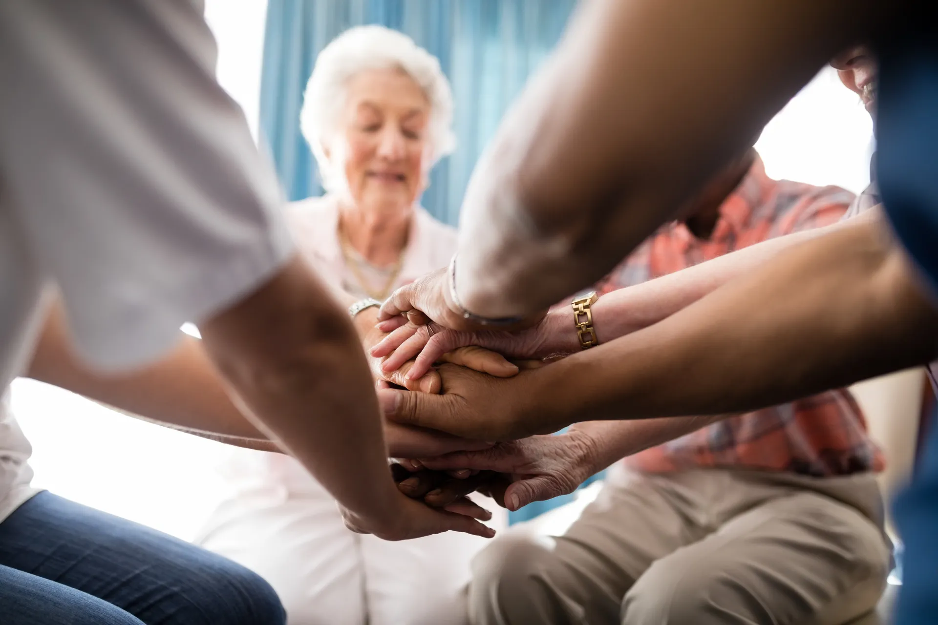 Older woman with white hair smiling while a caregiver holds her hand in a comfortable setting